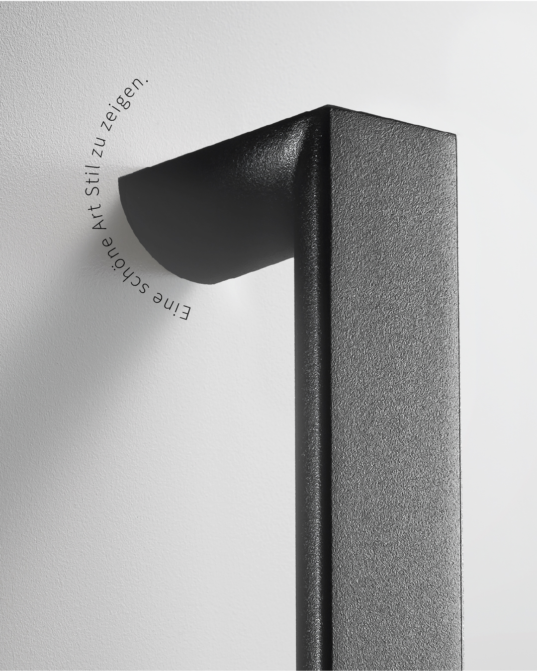 Detailaufnahme eines schwarzen, strukturierten, L-förmigen Stoßgriffs, Text: Eine schöne Art Stil zu zeigen. Design-Türgriff.