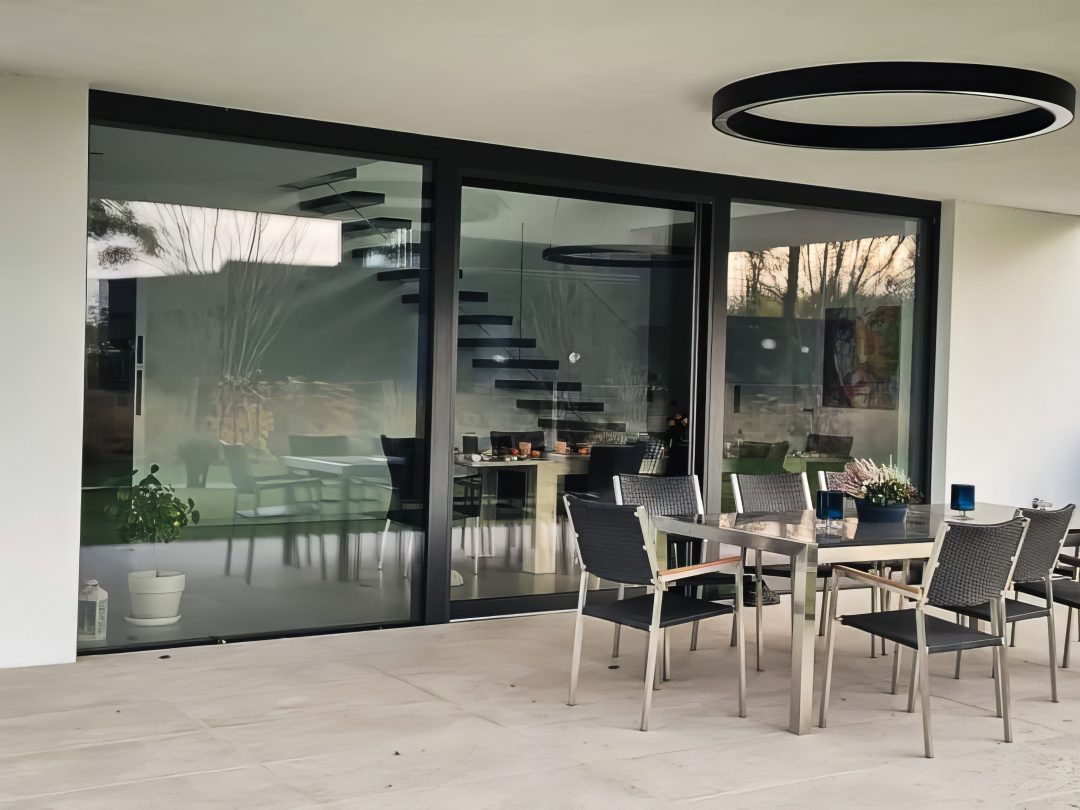 Nahaufnahme einer Hebe-Schiebetür aus Aluminium mit Blick auf eine moderne Innentreppe und einen stilvoll eingerichteten Essbereich.