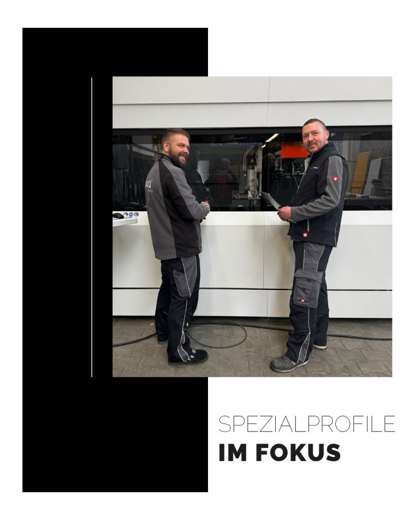 Zwei Mitarbeiter in Arbeitskleidung von Panz Aluminiumtechnik stehen lächelnd in einer Werkstatt vor einer modernen Produktionsanlage. Im Vordergrund steht das Design-Element 'Spezialprofile im Fokus'.