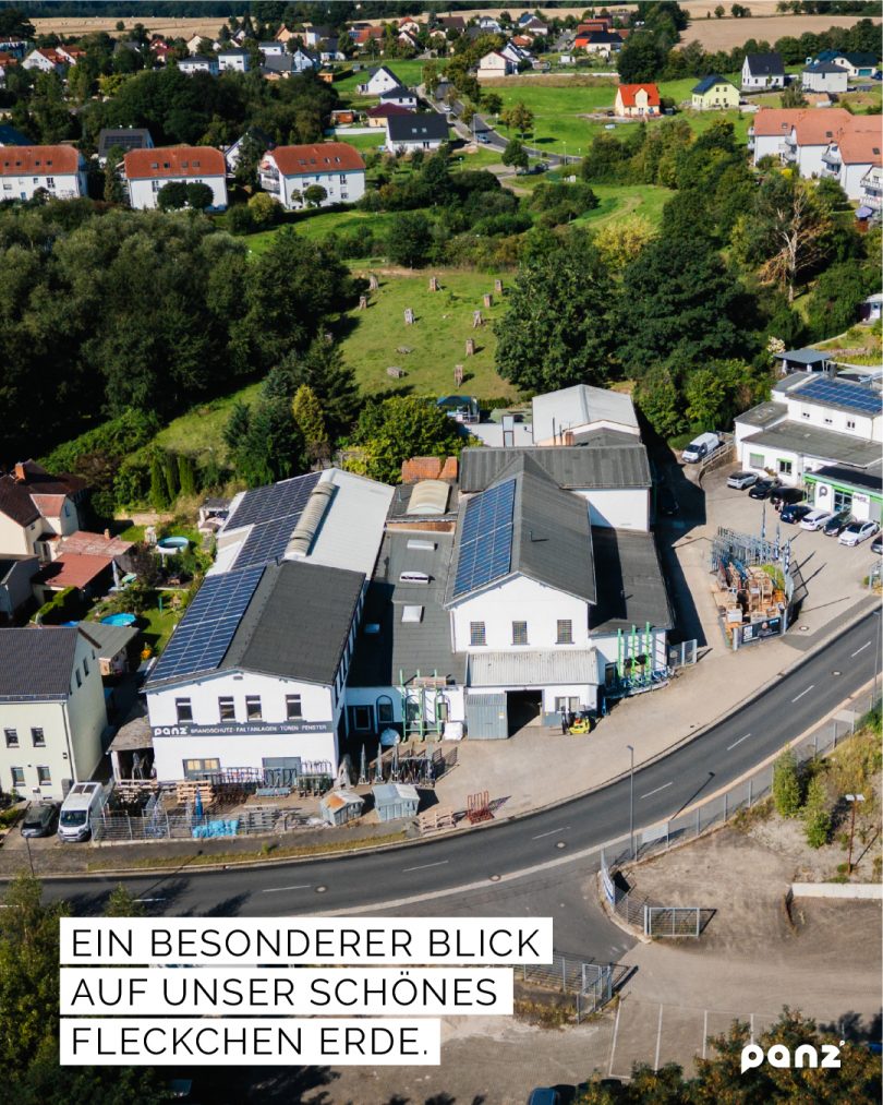 Luftaufnahme des Firmengeländes von Panz Aluminiumtechnik in Colditz, eingebettet in eine ländliche Wohn- und Naturlandschaft mit grünen Bäumen und Feldern im Hintergrund.