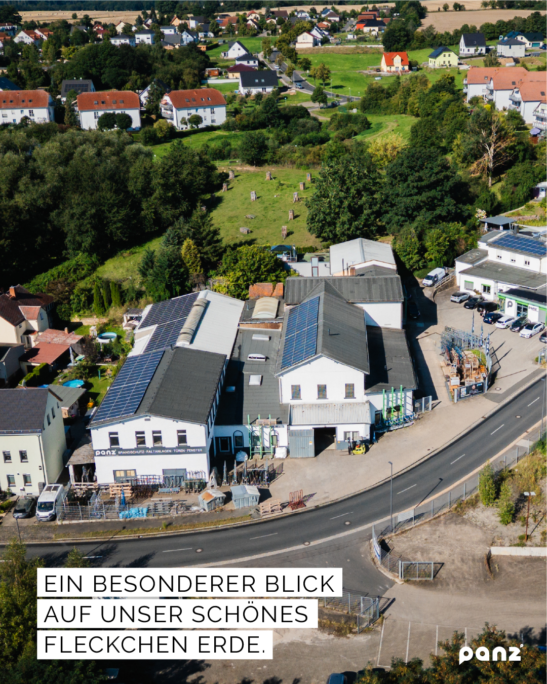 Luftaufnahme des Firmengeländes von Panz Aluminiumtechnik in Colditz, eingebettet in eine ländliche Wohn- und Naturlandschaft mit grünen Bäumen und Feldern im Hintergrund.