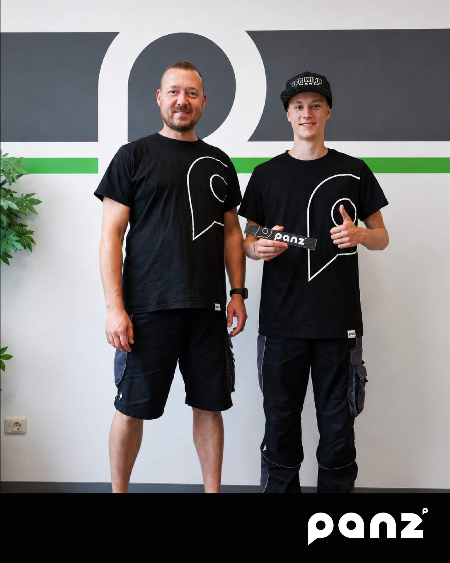 Auszubildender Tobias im schwarzen PANZ Team-Shirt mit Daumen nach oben neben seinem Kollegen vor dem Firmenlogo